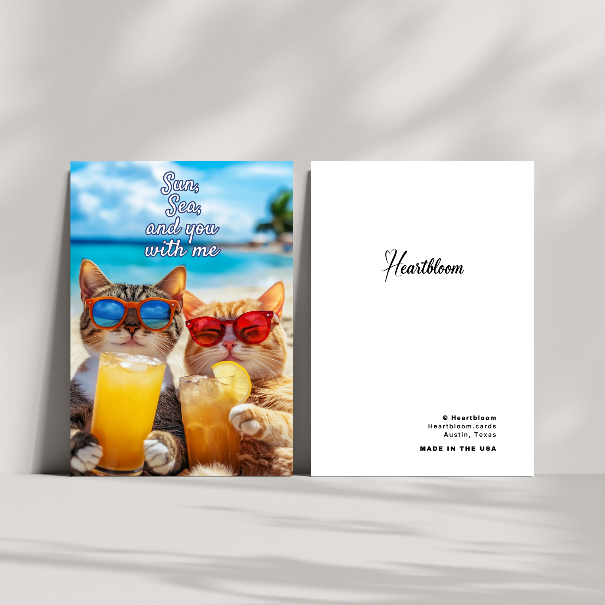 Card with two cats wearing sunglasses and drinking orange juice, set against a beach scene, with 'Heartbloom' branding.