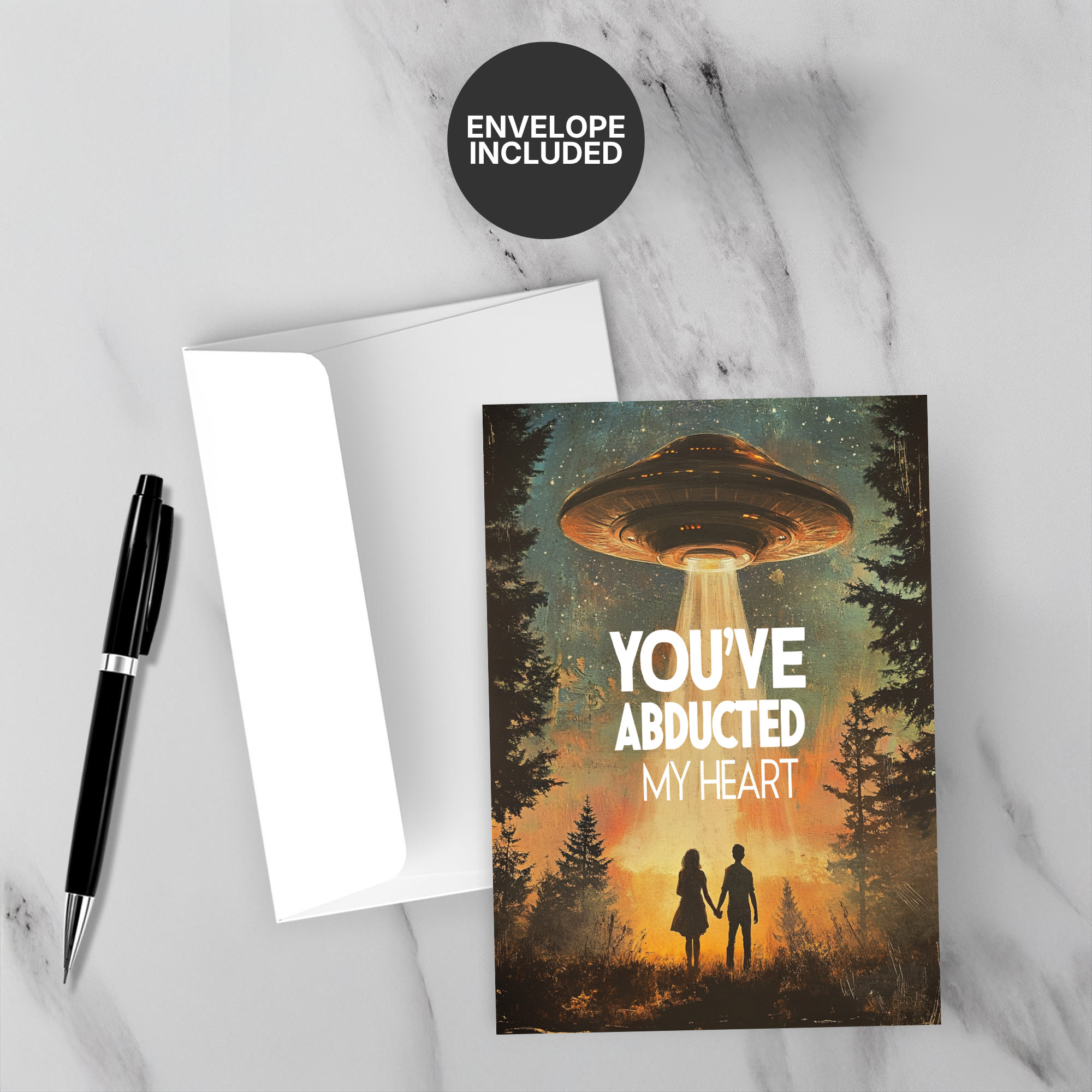 Greeting card with UFO design and 'You've Abducted My Heart' text on a marble surface with a pen and envelope.