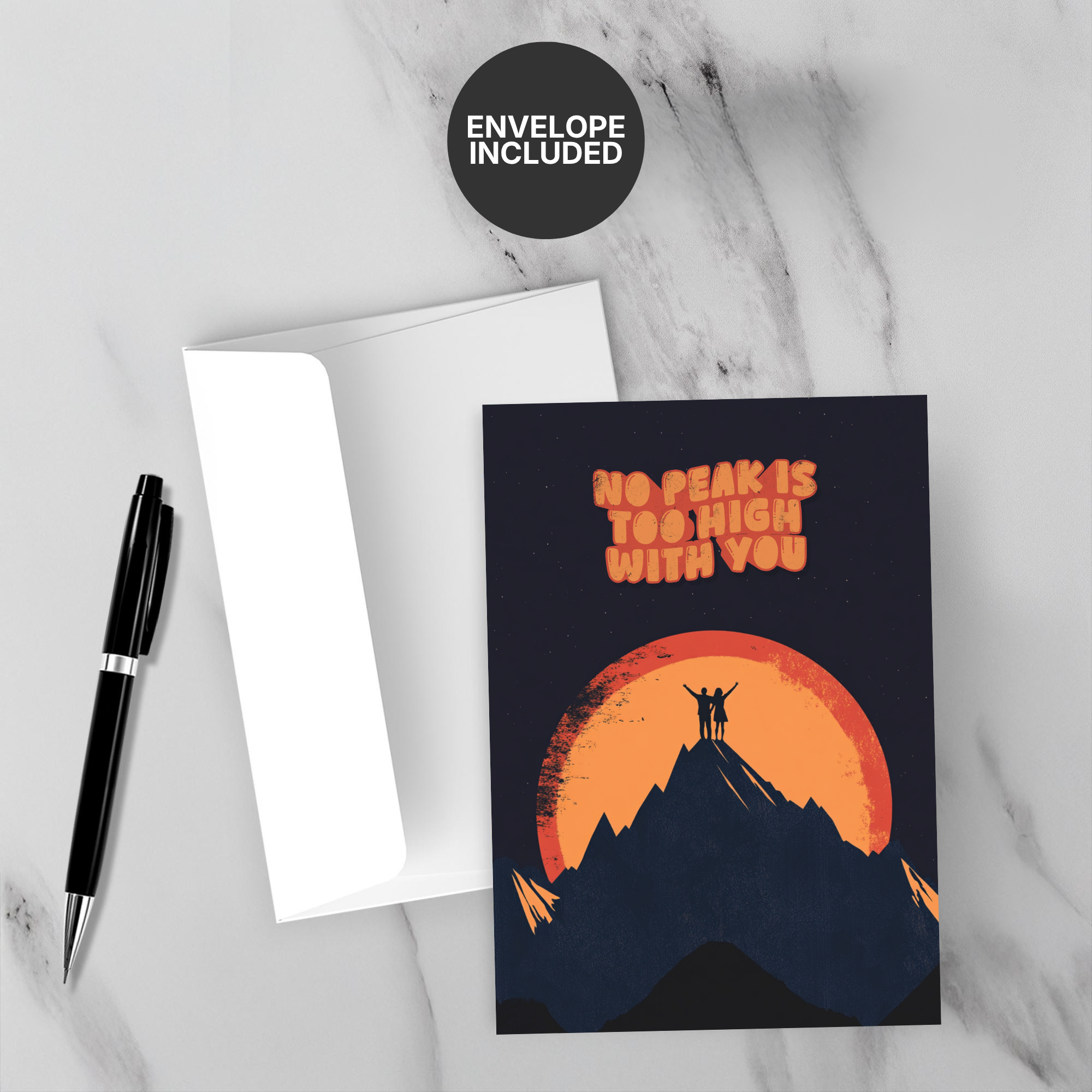 Greeting card with mountain and sunset design, 'No Peaks Too High With You' text, on a marble surface with a pen and envelope.