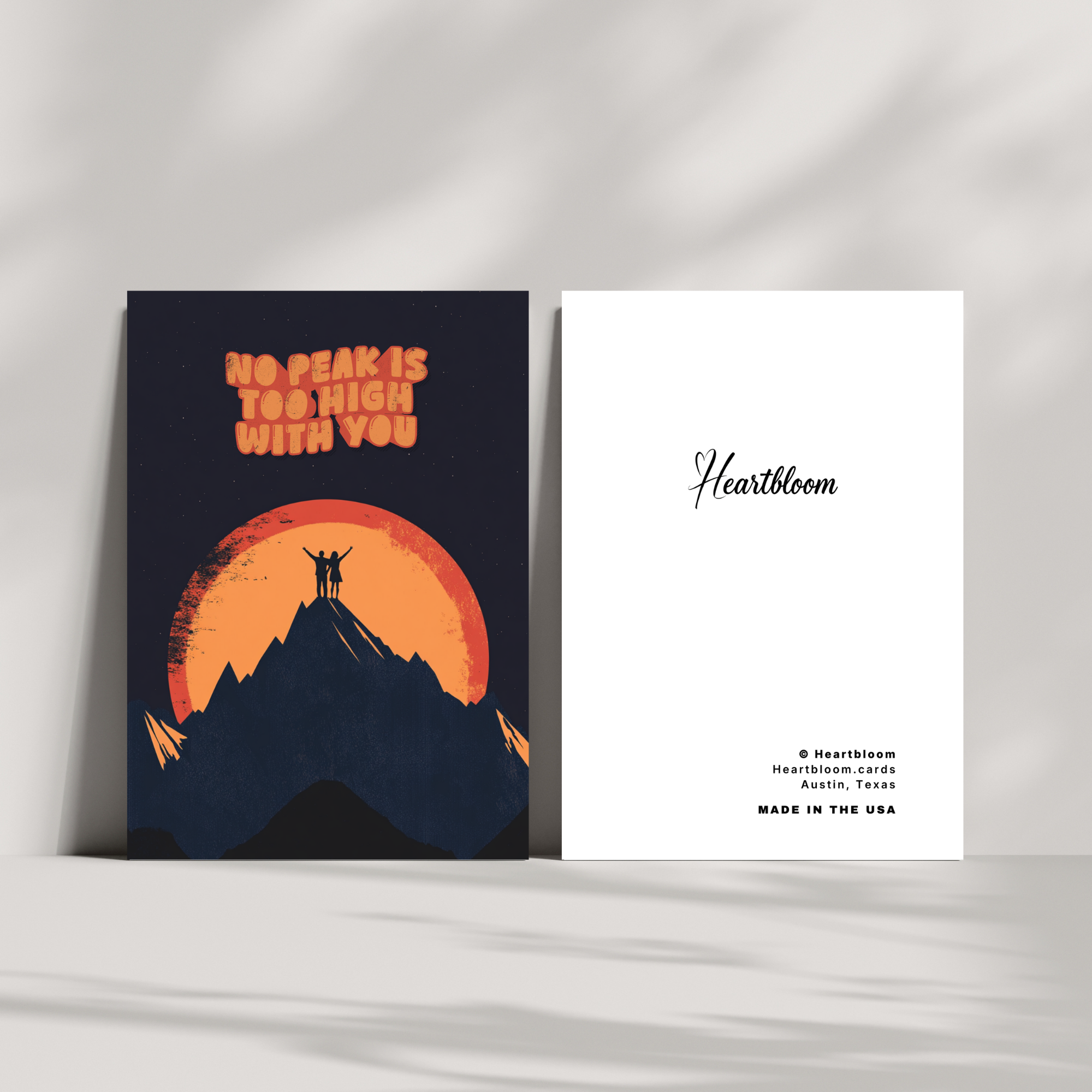 Two greeting cards with a mountain and sunset design on one and 'Heartbloom' branding on the other, against a light gray background.