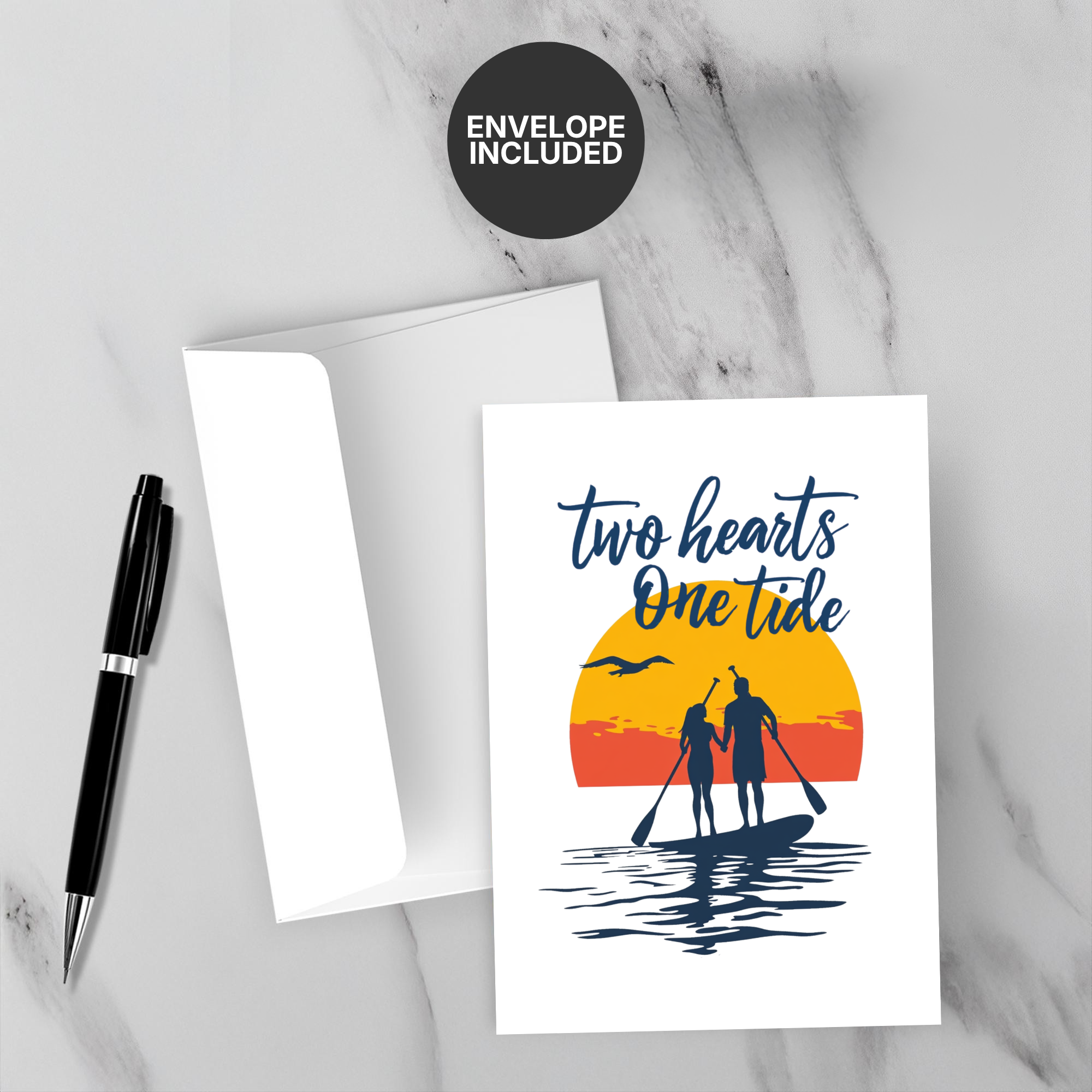 Greeting card with 'Two Hearts One Tide' design on a marble surface with a pen and envelope.