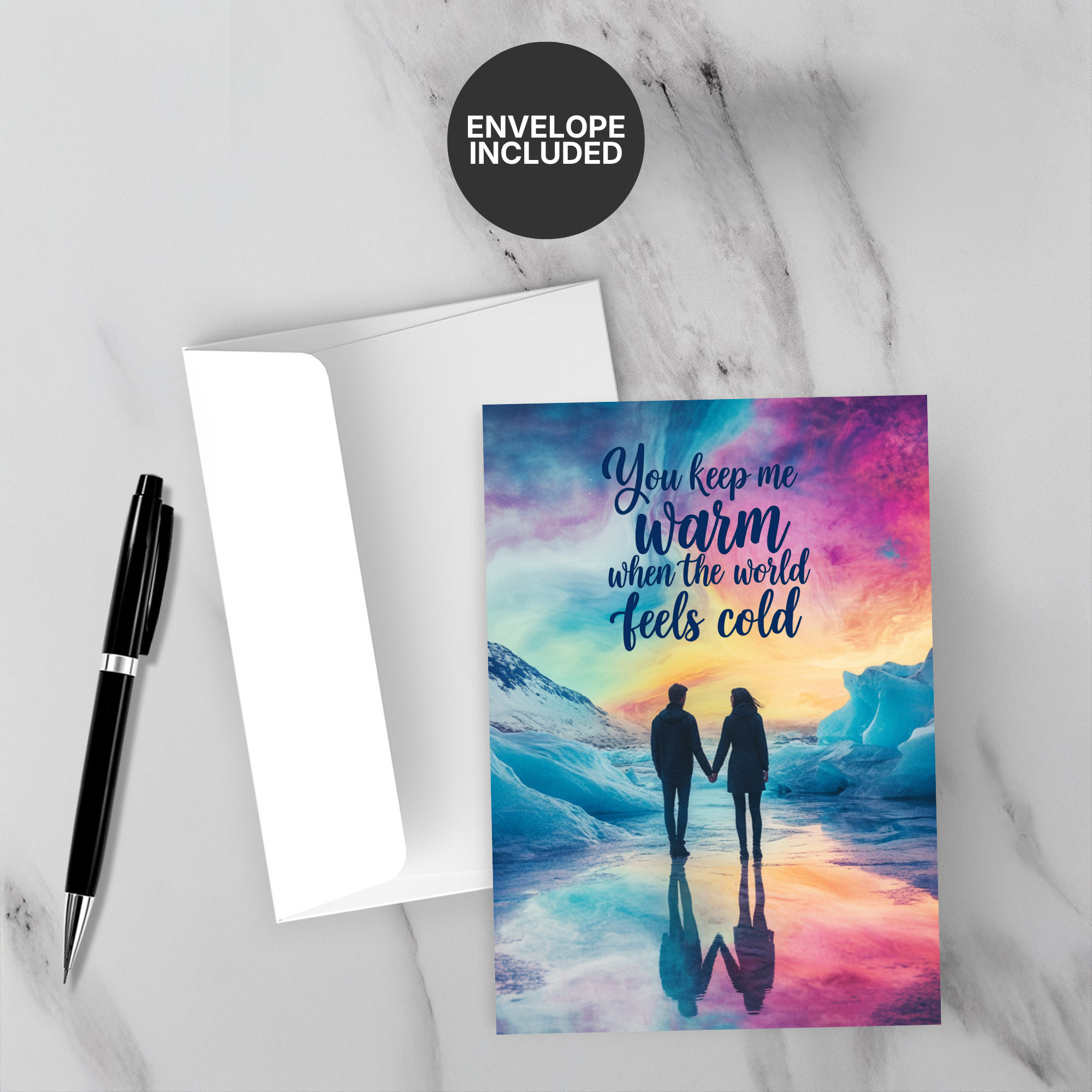 Greeting card with romantic design and 'You keep me warm when the world feels cold' text, accompanied by a pen and envelope on a marble surface.