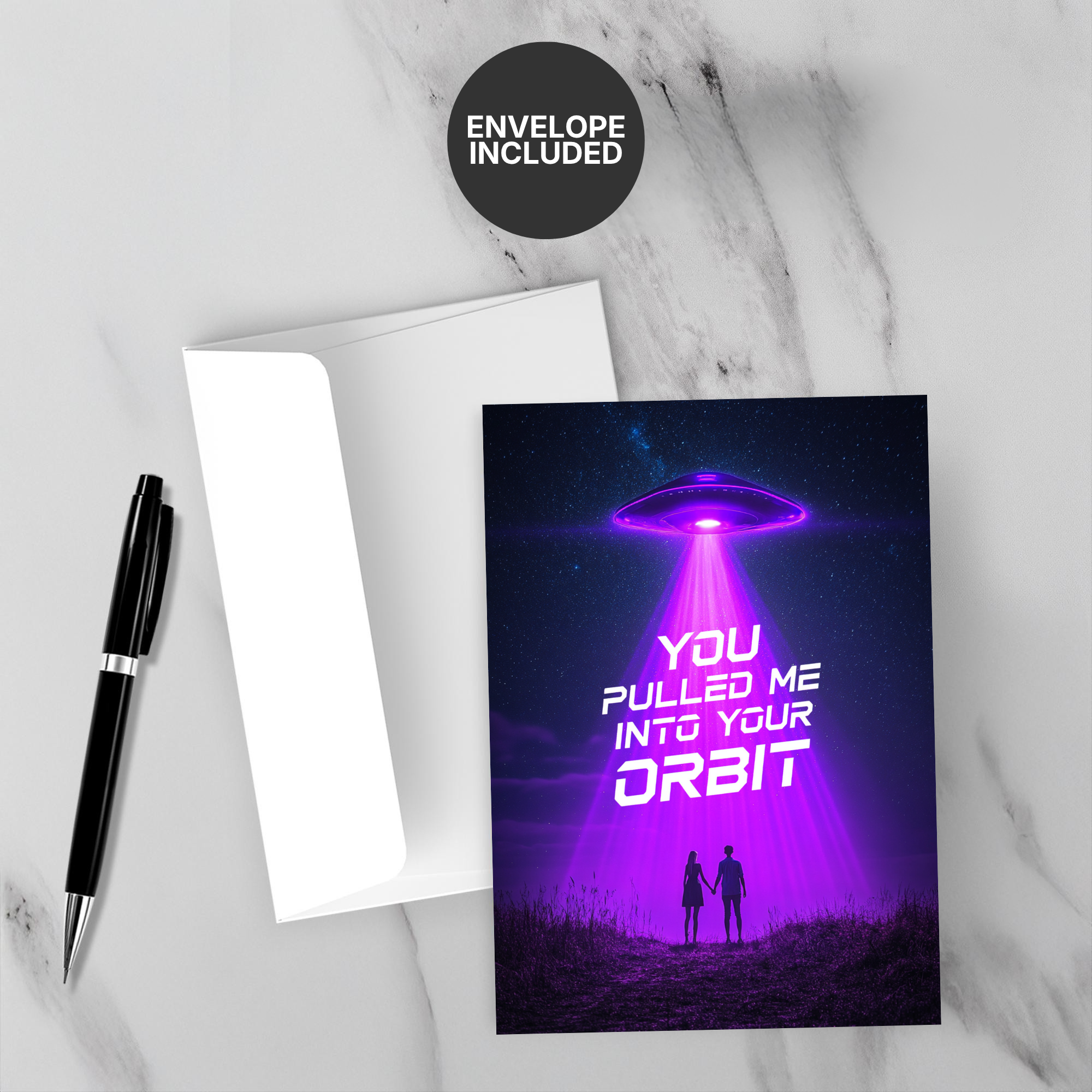 Greeting card with UFO design and text 'You pulled me into your orbit' on a marble surface with a pen and envelope.