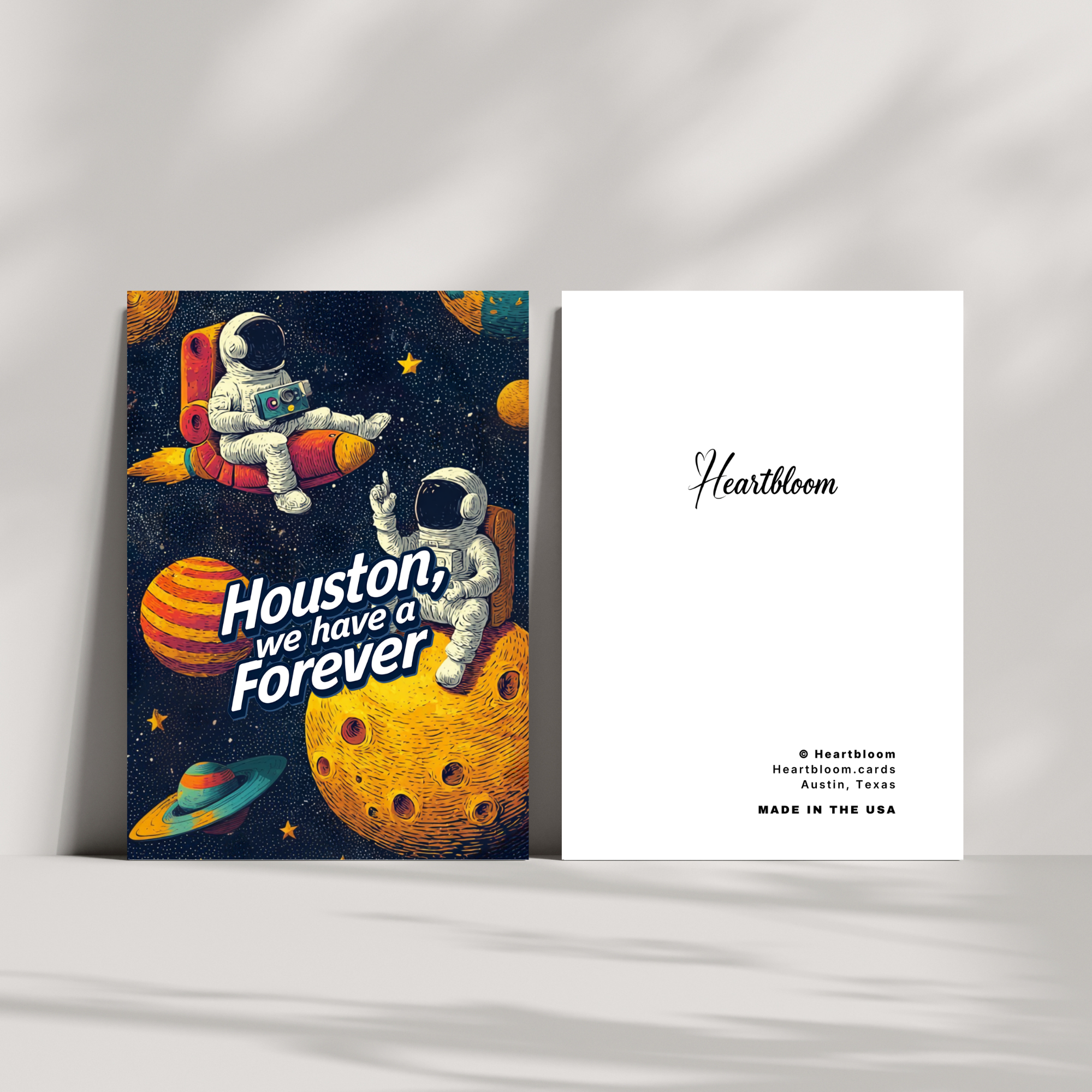 Space-themed greeting card with astronauts and 'Houston, we have a Forever' text, featuring the brand 'Heartbloom'.