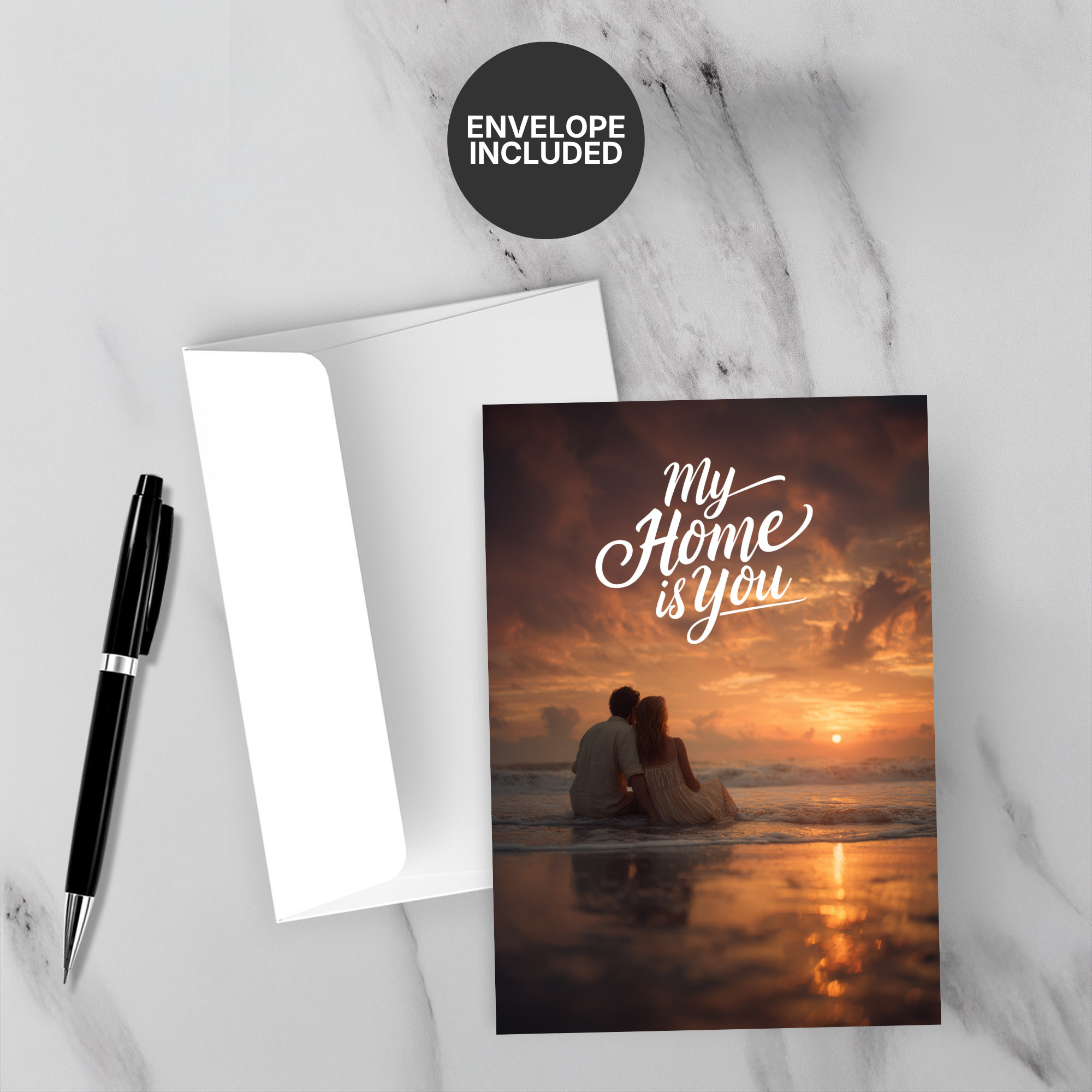 Greeting card with 'My Home is You' text and a couple on a beach at sunset, accompanied by a pen and envelope on a marble surface.