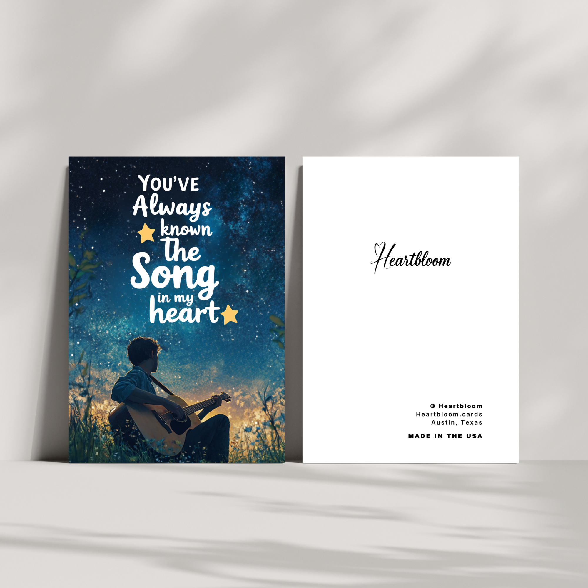 Card with silhouette of a person playing guitar against a starry night sky, featuring text 'You've Always Known The Song In My Heart' and 'Heartbloom' branding.