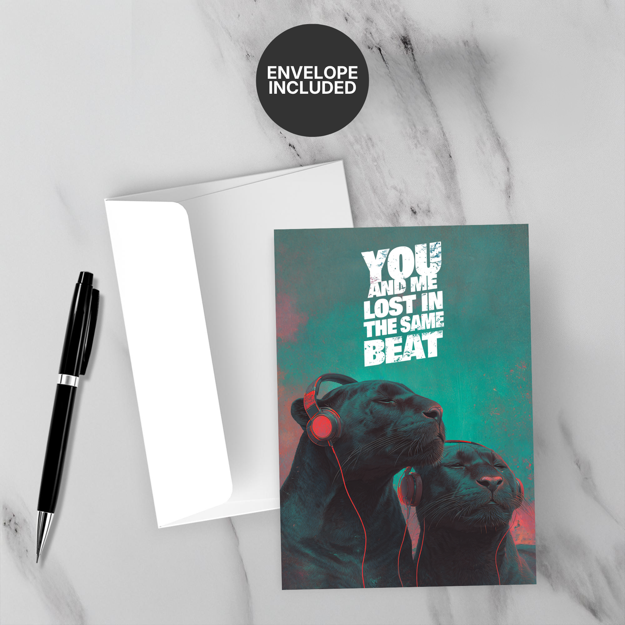 Greeting card with two black panthers wearing headphones and text 'You and me lost in the same beat' on a marble surface with a pen and envelope.