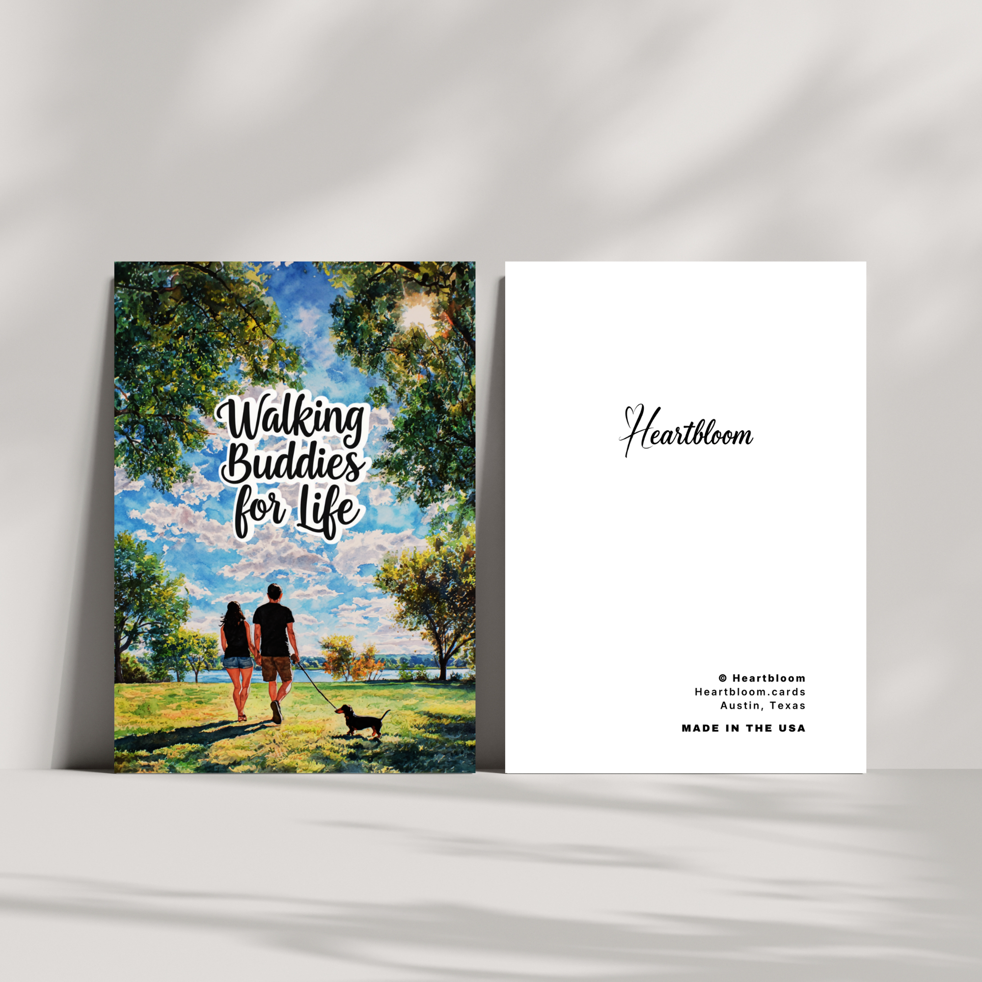Heartloom card with a couple walking a dog in a park and the brand name on a white background.