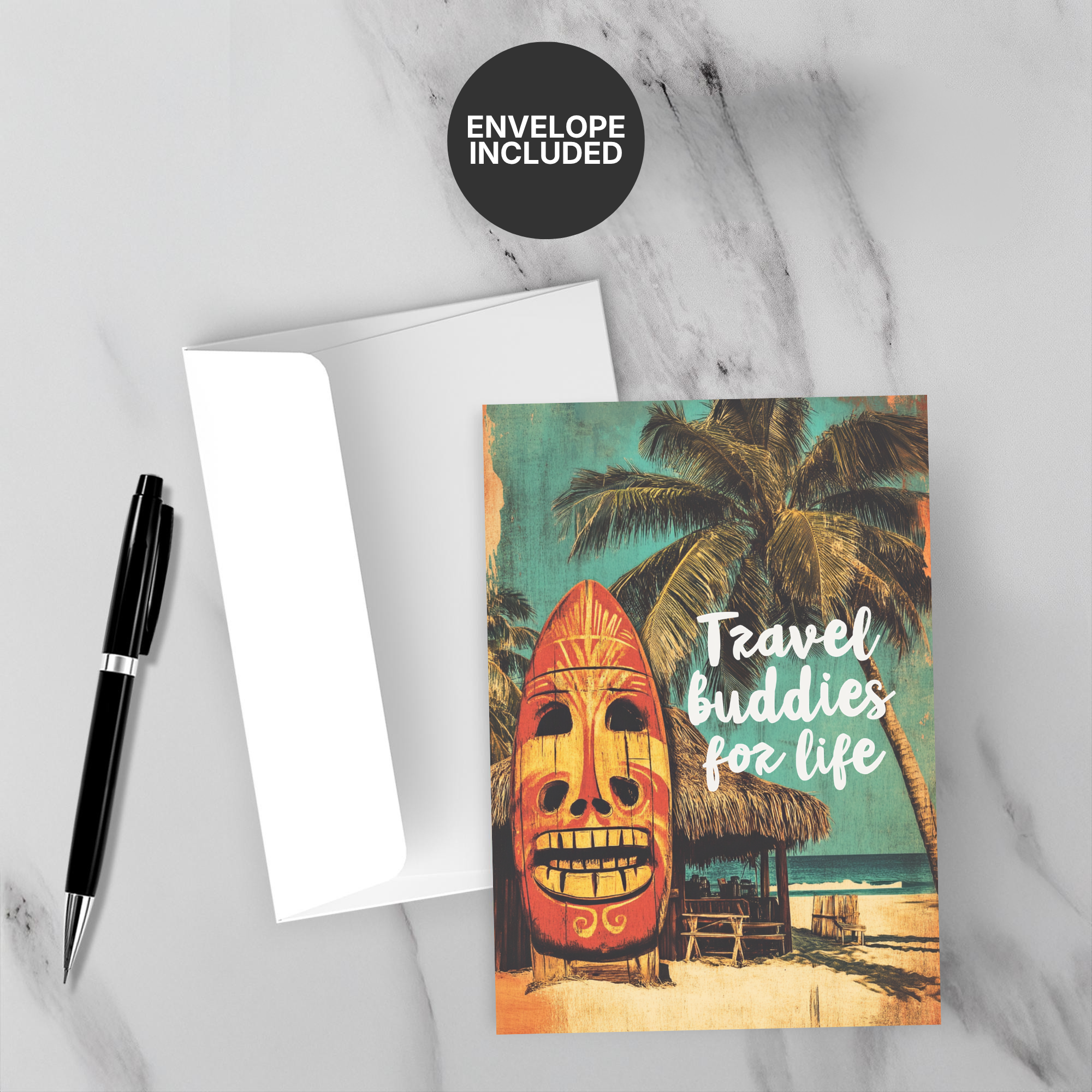 Greeting card with tropical design and 'Travel buddies for life' text, accompanied by a pen and envelope on a marble surface.