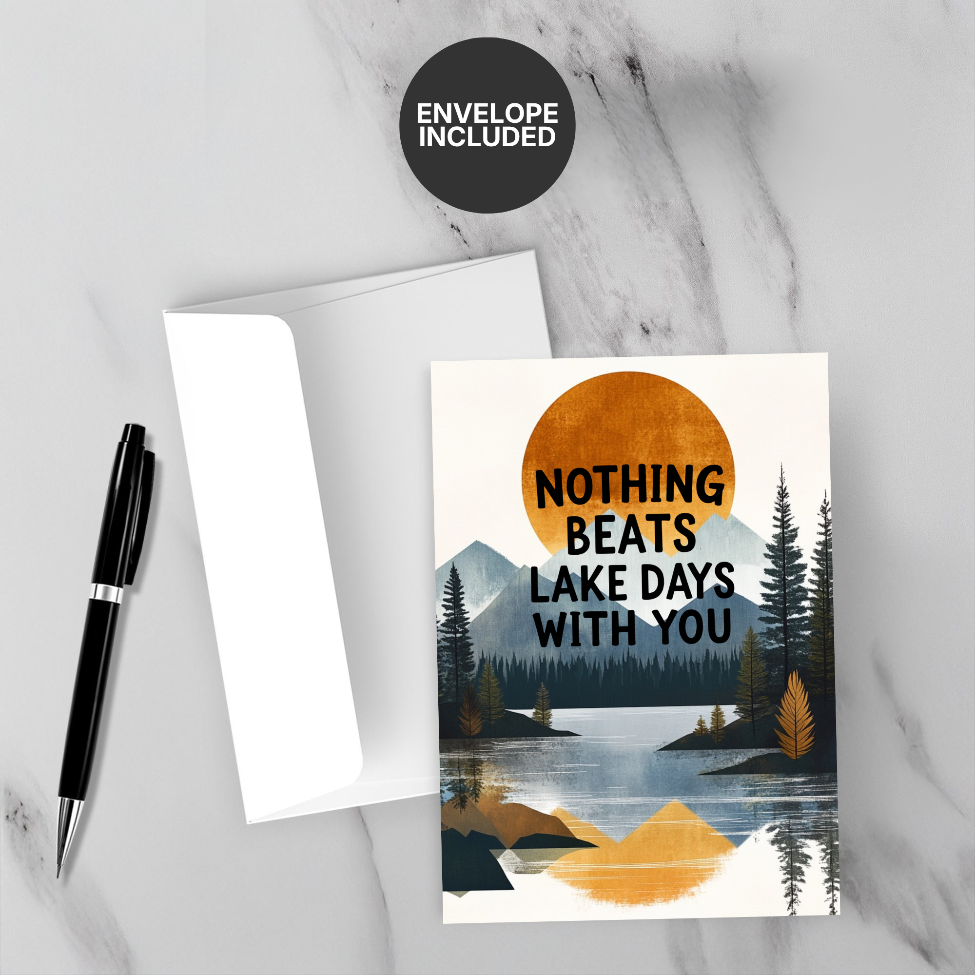 Greeting card with scenic design and 'Nothing Beats Lake Days With You' text, accompanied by a pen and envelope on a marble surface.