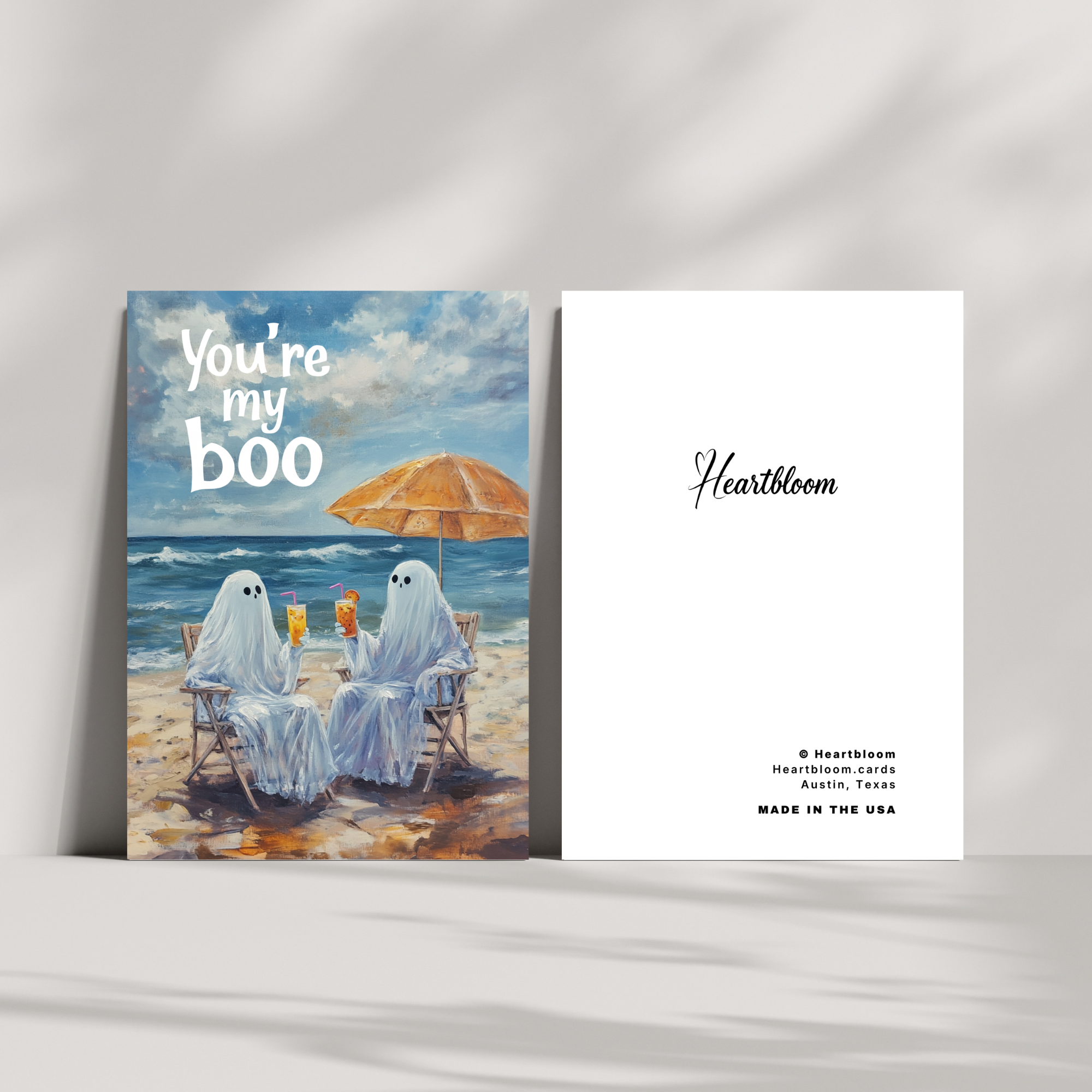 Card with ghosts on a beach under an umbrella, featuring 'You're my boo' text, on a white background.