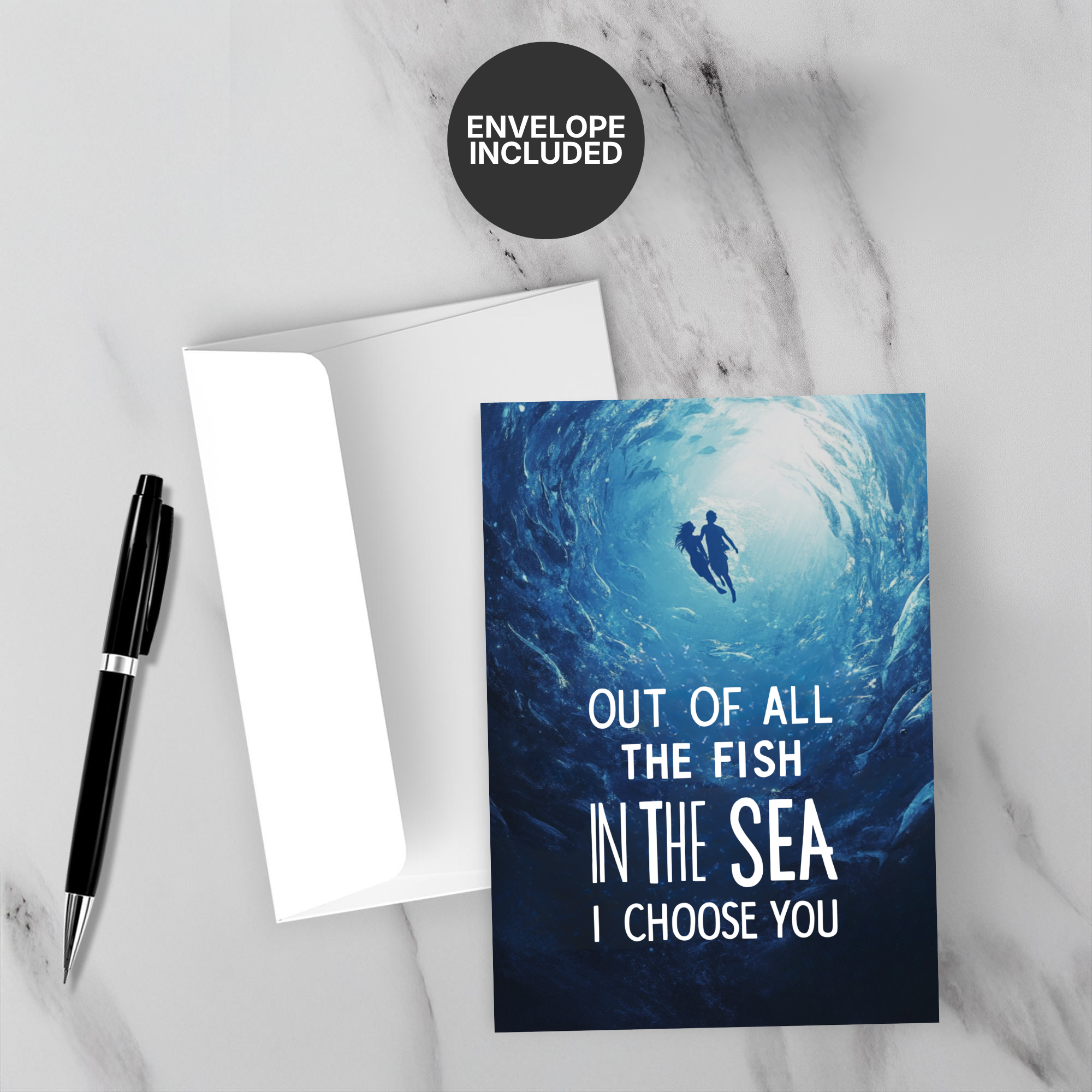 Greeting card with underwater scene and romantic text, accompanied by a pen and envelope on a marble surface.