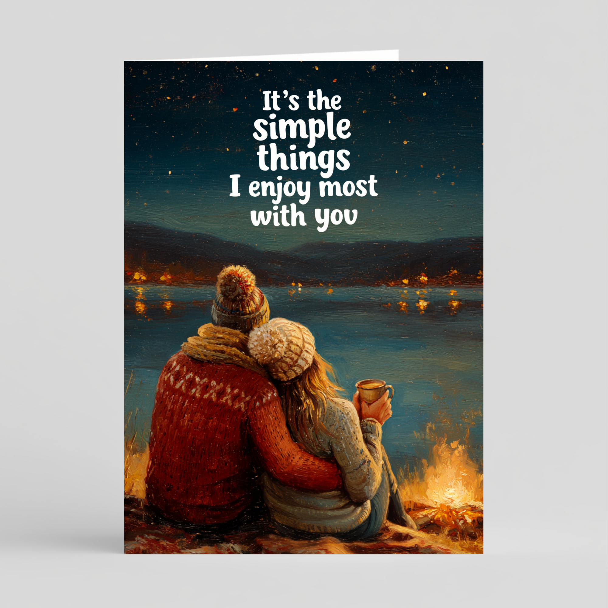 Card of a couple by a campfire with a romantic quote against a night sky over water.